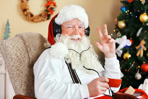 Santa Claus sitting with Digital tablet in comfortable chair near Christmas tree at home