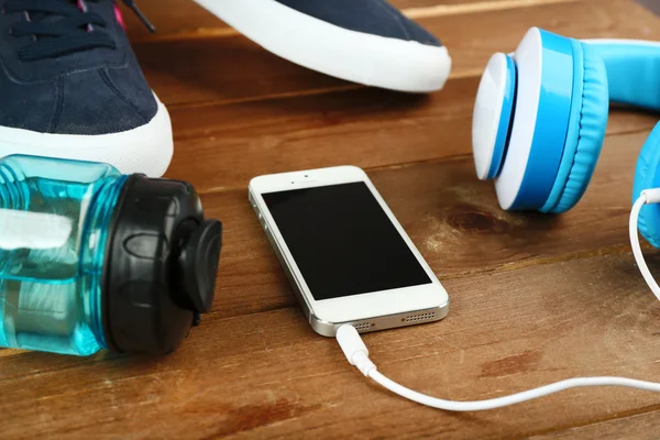 Sport shoes with bottle of water and headphones on wooden background