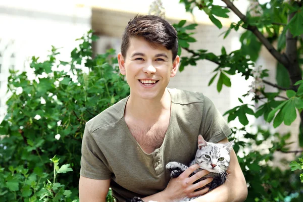 Handsome young man with cute cat outdoors