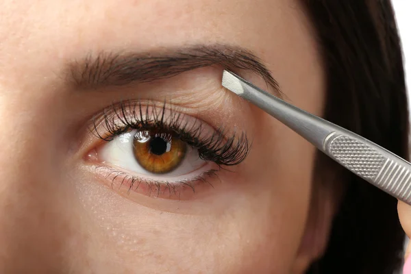 Young woman plucking eyebrows with tweezers close up