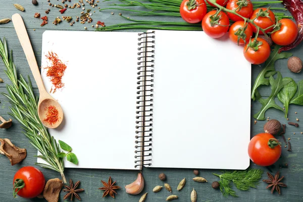 Open recipe book with fresh herbs, tomatoes and spices on wooden background