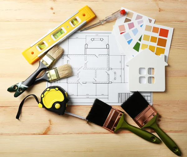 Construction instruments, plan and brushes on wooden table background