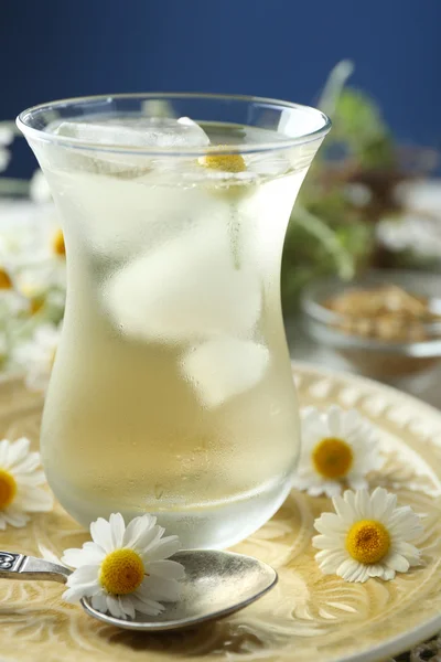Glass of cold chamomile tea with ice cubes and chamomile flowers on table, on colorful background