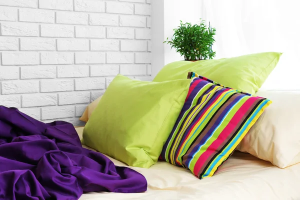 Comfortable bed with colorful pillows and purple blanket in bedroom