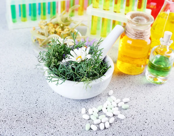 Herbs in mortar, test tubes and pills, on table, on light background