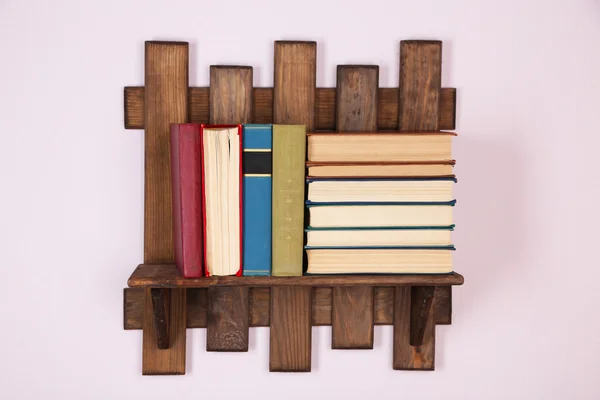 Wooden shelf with books on wall