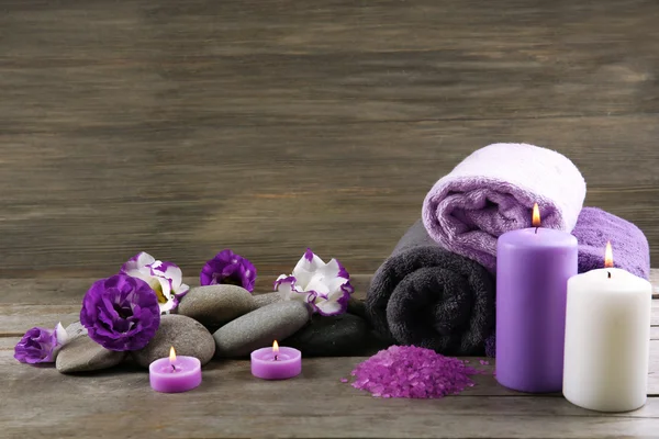 Spa still life with towels, purple flowers and candlelight on wooden background