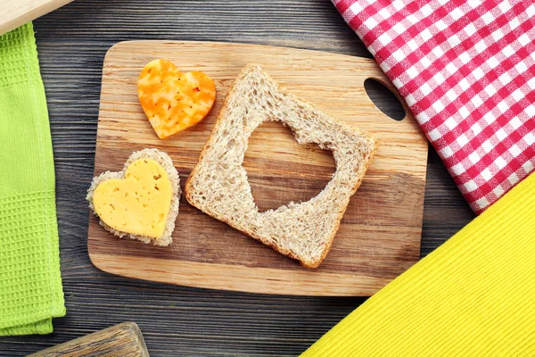 Bread slice with cut in shape of heart and cheese on table close up