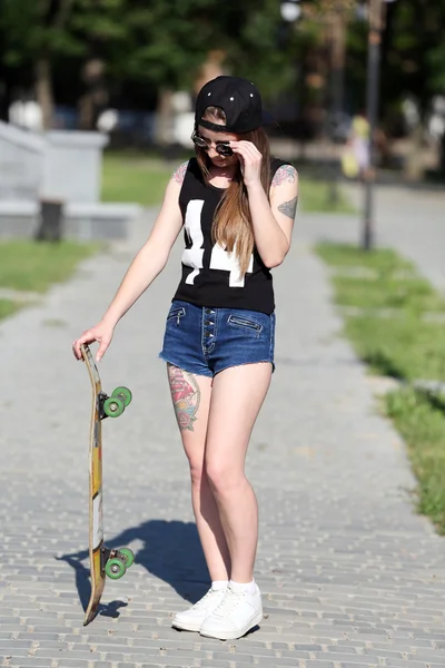 Beautiful tattooed girl with skateboard, outdoors