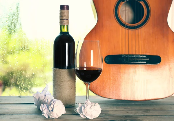 Acoustic guitar and glass of wine next the window with rain drops