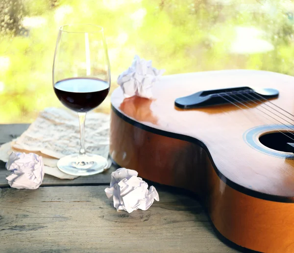Acoustic guitar and glass of wine next the window with rain drops