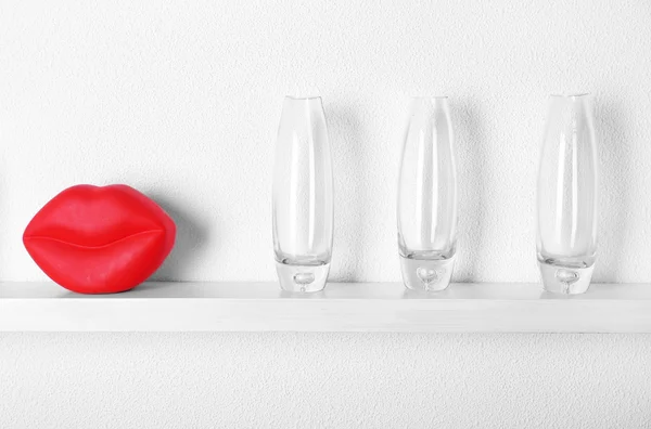 Decorative glass vases with red lips on wooden shelf  on white wallpaper background