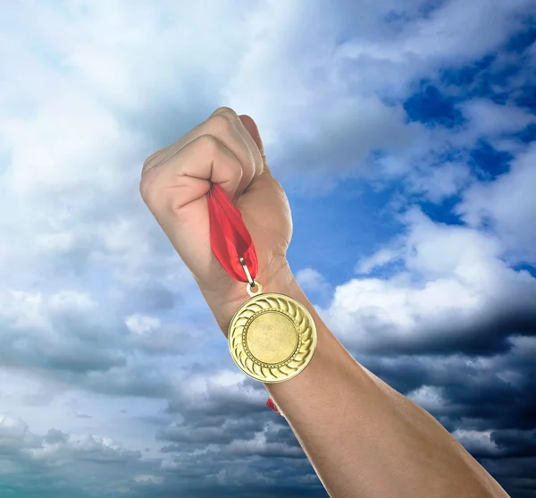 Golden medal in hand on sky background