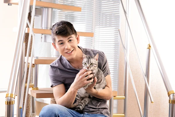 Handsome young man with cute cat sitting on steps at home