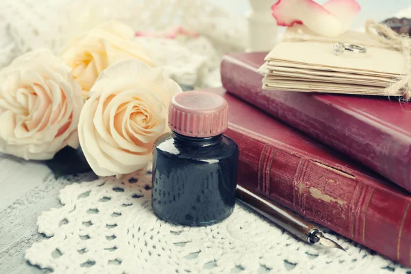 Fresh roses with old book and letters on color wooden table, on light background. Vintage concept