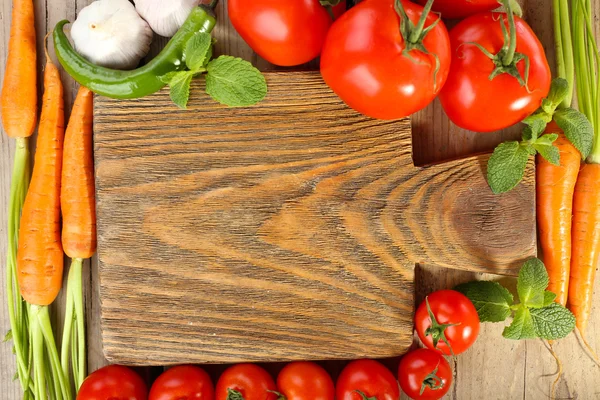 Fresh vegetables with cutting board on wooden table, top view