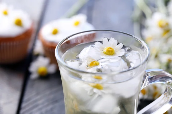 Cup of chamomile tea with chamomile flowers and tasty muffins on color wooden background