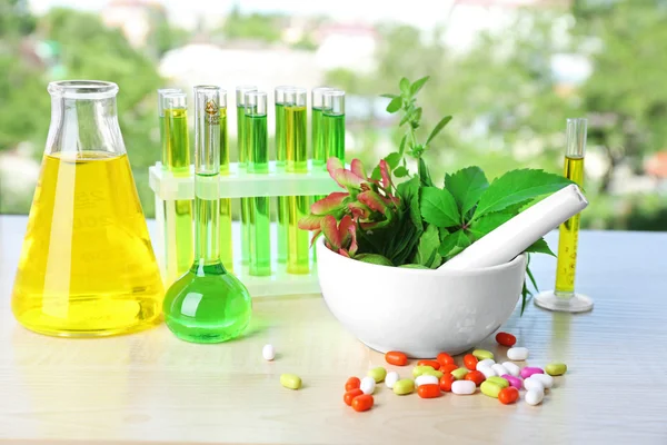 Herbs in mortar, test tubes and pills, on table, on bright background