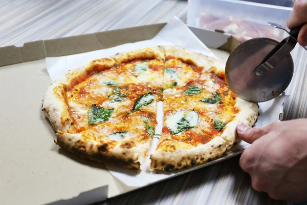 Male hand cutting pizza with blade pizza in box, closeup