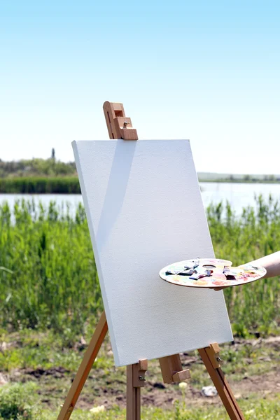 Female hand holding palette and easel with canvas outdoors