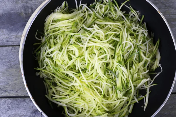 Grated zucchini and squash in pan on wooden table close up