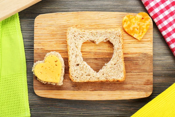 Bread slice with cut in shape of heart and cheese on table close up