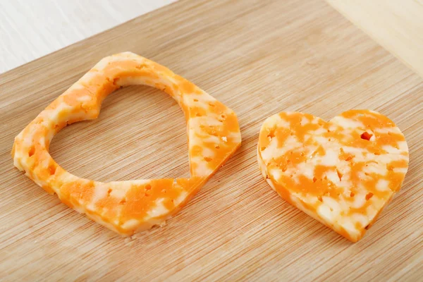 Cheese slice with cut in shape of heart on wooden background