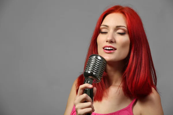 Beautiful young woman with microphone on gray background