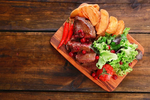 Beef with cranberry sauce, roasted potato slices on cutting board, on wooden background