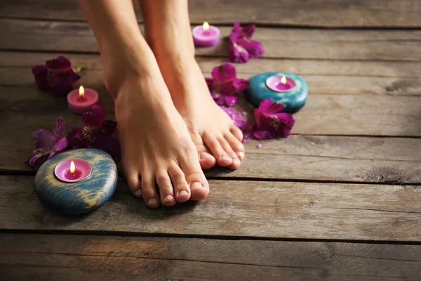 Female feet at spa pedicure procedure with flowers and candlelight on wooden background