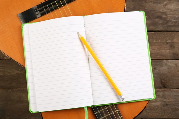 Music recording scene with guitar and memo pad on wooden table, closeup