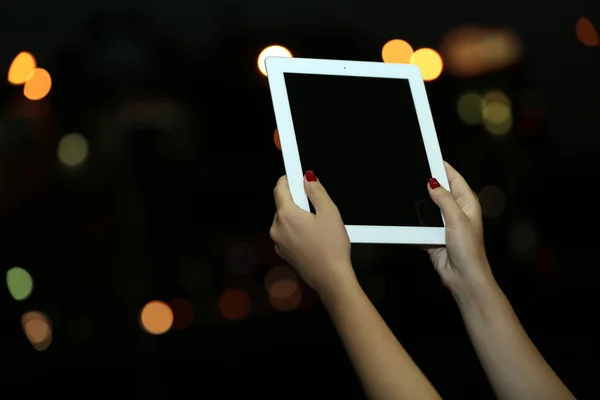 Female hand holding touch screen tablet on blurred night lights background
