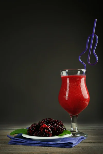 Glass of blackberry smoothie on wooden table on grey background