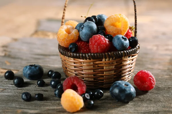 Sweet tasty berries in basket on wooden table close up