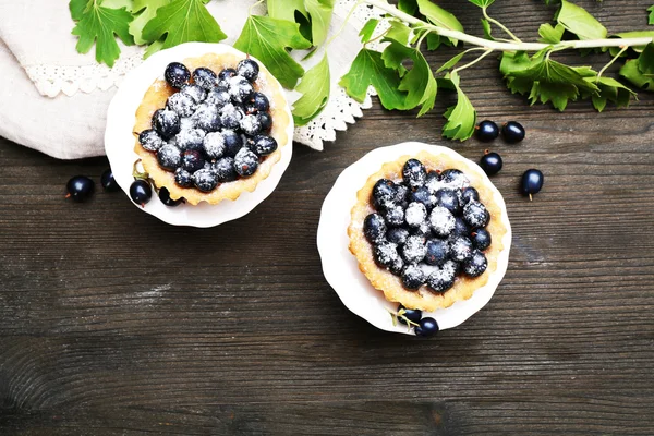 Delicious crispy tarts with black currants on white stand on wooden table, top view