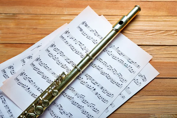 Silver flute with music notes on wooden table close up