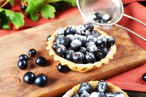 Delicious crispy tart with black currants on wooden cutting board, closeup