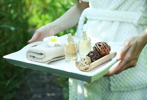 Female hands with tray of spa products over green reeds on river