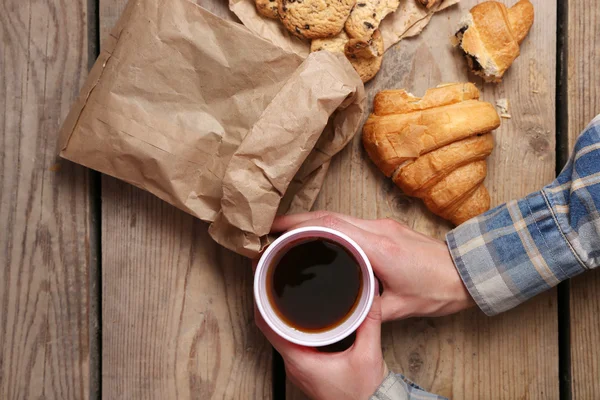 Female hands holding cup of coffee and cookies on wooden table close up