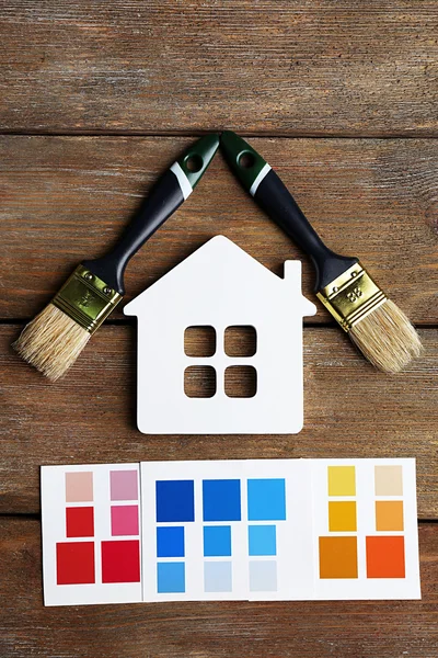 Colorful paint samples, decorative house  and paintbrushes on wooden table background