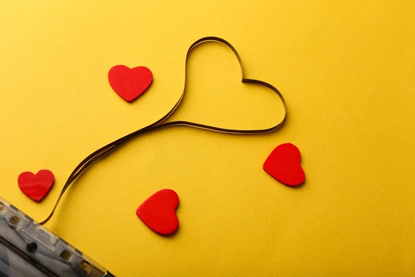 Audio cassette with magnetic tape in shape of heart on yellow background