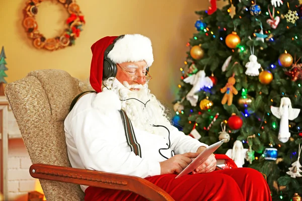 Santa Claus sitting with Digital tablet in comfortable chair near Christmas tree at home