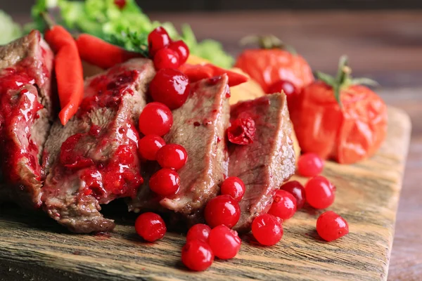 Beef with cranberry sauce, roasted potato slices on cutting board, on wooden background