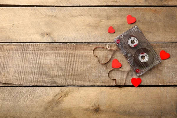 Audio cassette with magnetic tape in shape of hearts on wooden background