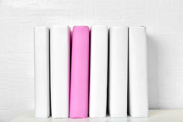 Blank books and pink one on shelf on white wallpaper background