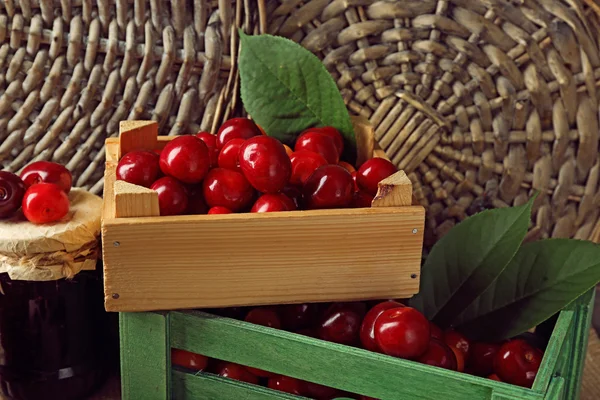 Sweet cherries with green leaves  in basket and wooden boxes, on wooden background