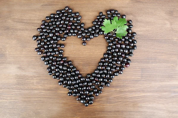 Black Currant in shape of heart on wooden background