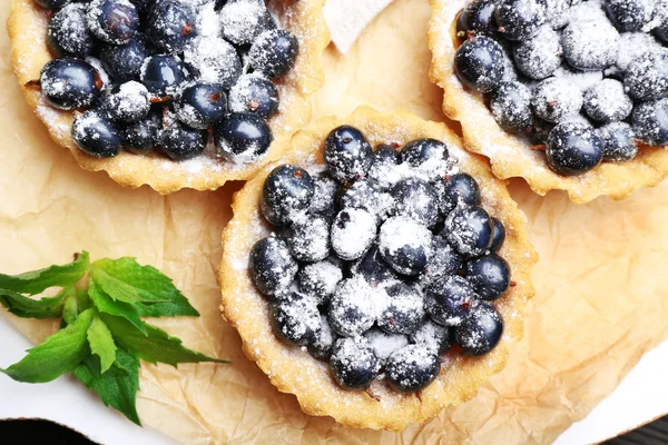 Delicious crispy tarts with black currants on parchment, top view