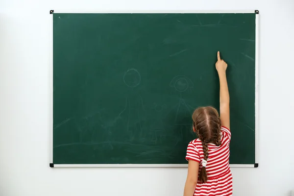 Little girl pointing at something on chalkboard