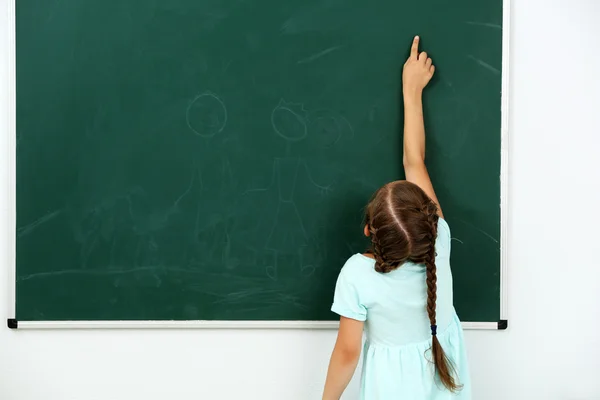 Little girl pointing at something on chalkboard